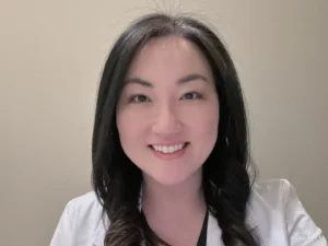 A woman with long dark hair wearing a white lab coat smiles at the camera.