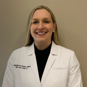 A woman wearing a white lab coat with embroidery reading "Stephany Steen, MSN, FNP-BC, FNP-C" smiles against a beige background.